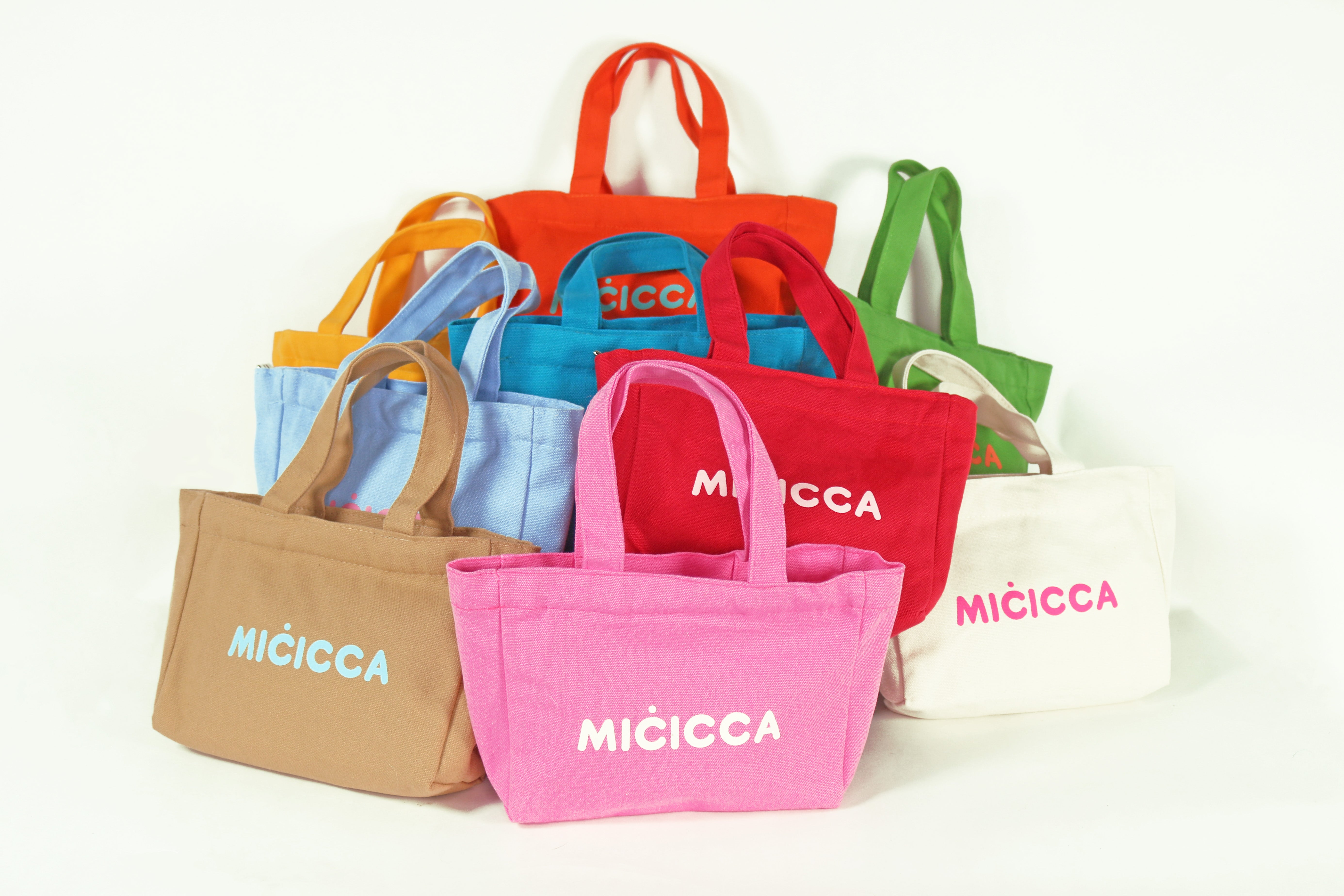 Colorful tote bags showcasing the word micicca in bold letters, arranged together for display.