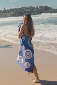 Blue tie-dye shibori sand-free beach towel draped over a woman walking along the shoreline