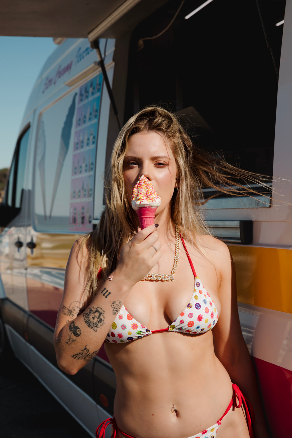 A woman in a bikini savors an ice cream cone, smiling under the warm sun at the beach.